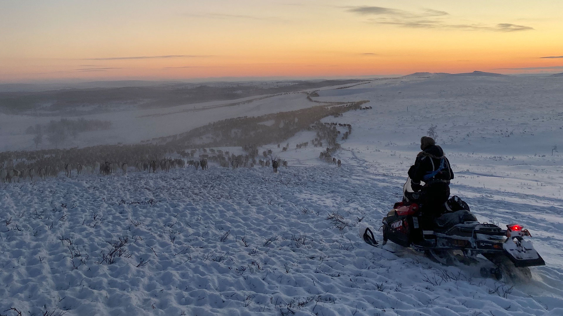 Man on vehicle at the top of hill. The landscape is covered in snow 