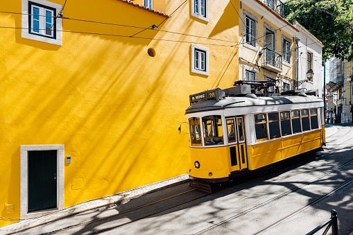 Yellow tram moving past yellow building in Lisbon, Portugal
